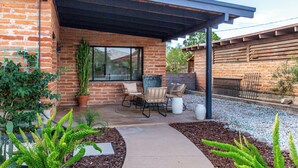 A patio area with a brick wall, a pergola, outdoor furniture, and various plants. - 3 bedroom Mid Century home with easy access to everything! Pet friendly! (Tucson)
