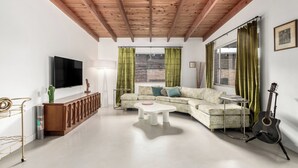A living room with a wooden ceiling, a flat-screen TV, a sofa, a coffee table, a guitar, and a cactus decoration. - 3 bedroom Mid Century home with easy access to everything! Pet friendly! (Tucson)