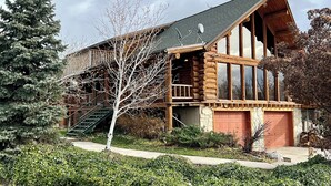 Une cabane en rondins avec un toit à forte pente, une terrasse en bois et un escalier menant à l’entrée.