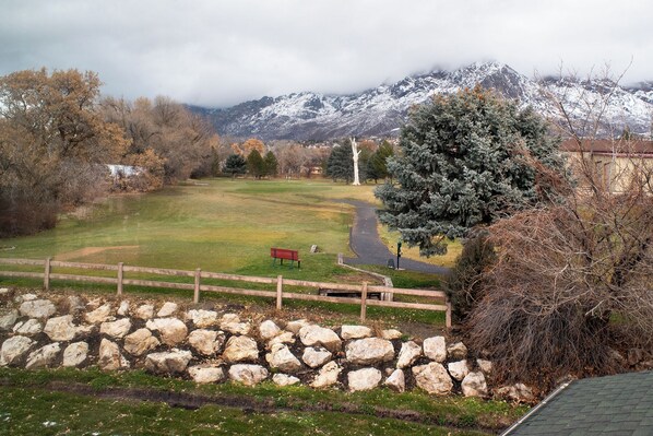 Un parque con un muro de piedra, una valla de madera y un sendero que lleva a un banco.