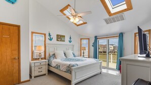 Une chambre à coucher comprenant un lit, un bureau, une chaise, un ventilateur de plafond et une vue sur l’extérieur.