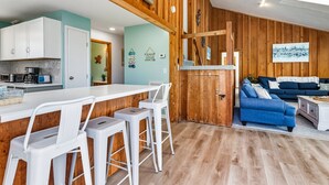 Une cuisine moderne avec des meubles blancs, un îlot central en bois doté de tabourets de bar, et un canapé bleu dans l’espace salon.