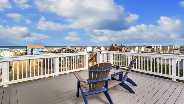 Une terrasse offrant une vue sur la plage et l’océan, avec une chaise en bois et une table.