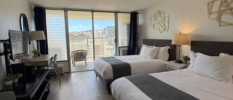 Habitación de hotel con dos camas, un escritorio, una silla y un amplio ventanal con vistas a la ciudad.