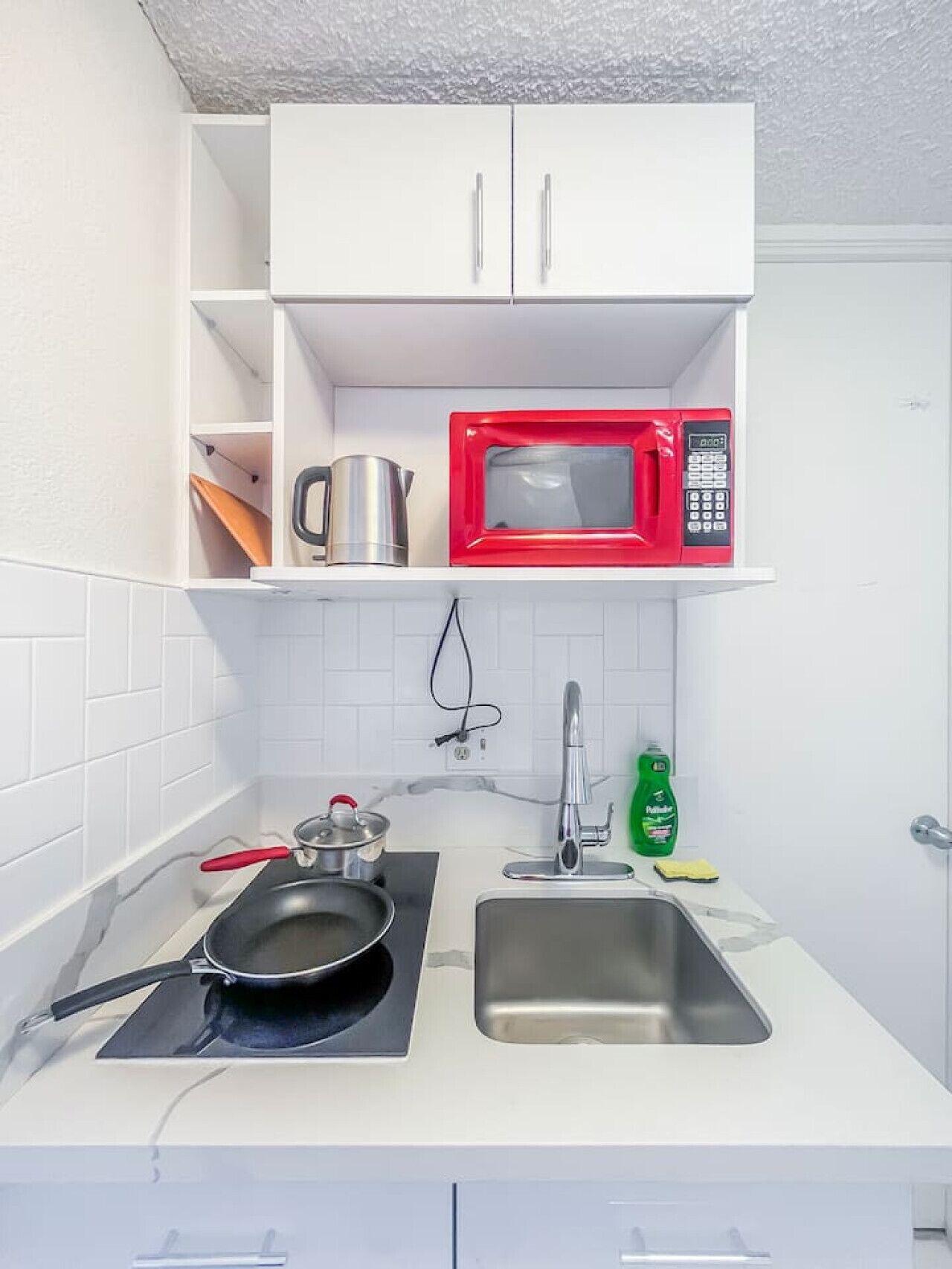 A compact kitchen with white cabinets, a red microwave, a sink, and a stovetop.