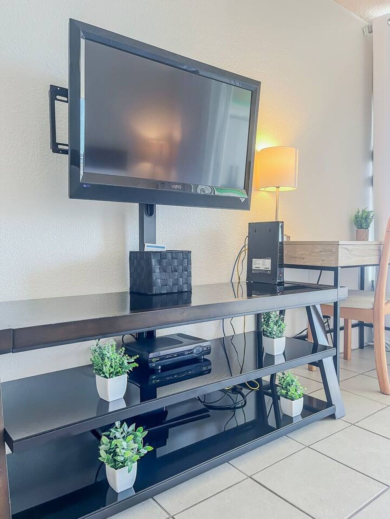 Ett modernt vardagsrum med en väggmonterad platt-TV, en mörk möbel för underhållningsutrustning med flera hyllor och ett litet bord med en lampa.