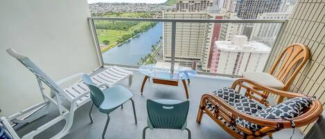 A balcony with a view of a river and cityscape, furnished with chairs and a table.