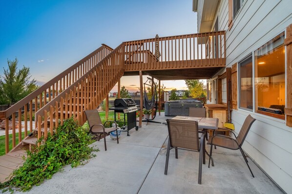 A covered patio with a wooden staircase, outdoor seating, and a grill area.