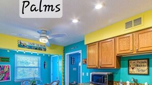 A kitchen with teal walls, wooden cabinets, a stainless steel dishwasher, and a microwave. - Port Canaveral/Space X- steps from beach 2-bedroom colorful unit w/ AC-sleeps 8 (Cocoa Beach)