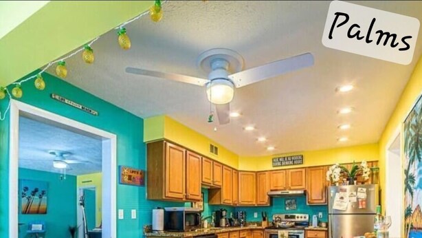A kitchen with wooden cabinets, a dining area with wicker chairs, and a ceiling fan. - Port Canaveral/Space X- steps from beach 2-bedroom colorful unit w/ AC-sleeps 8 (Cocoa Beach)