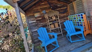 A rustic wooden structure with a thatched roof, two blue Adirondack chairs, and a shelf with colorful plastic containers. - Port Canaveral/Space X- steps from beach 2-bedroom colorful unit w/ AC-sleeps 8 (Cocoa Beach)