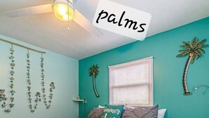 A bedroom with teal walls, a bed with a grey duvet, and decorative palm tree wall art. - Port Canaveral/Space X- steps from beach 2-bedroom colorful unit w/ AC-sleeps 8 (Cocoa Beach)