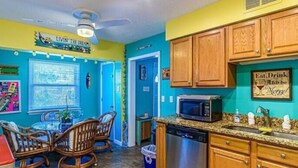 A kitchen with teal walls, wooden cabinets, a stainless steel dishwasher, and a microwave. - Port Canaveral/Space X- steps from beach 2-bedroom colorful unit w/ AC-sleeps 8 (Cocoa Beach)