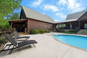 A wooden cabin with a pool, lounge chairs, and a covered patio area. - Heated Pool, Sleeps 30, 6,000 sq ft. Family Cabin, Arcade, Pool Table, Bunk Room (Broken Bow)
