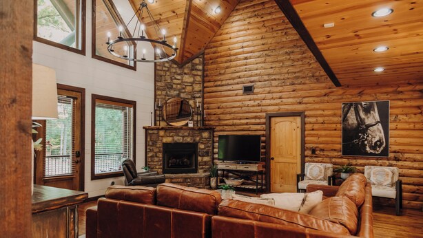 L’intérieur d’une cabane en rondins, avec une cheminée en pierre, un canapé en cuir et un téléviseur.