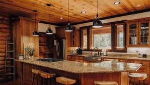 Une cuisine dotée de meubles en bois, de plans de travail en granit, de tabourets de bar et de luminaires suspendus.