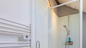 A modern bathroom with a glass shower enclosure, a white towel rack, and a small shelf with toiletries. - Le Saint-Loup - DRACY SAINT LOUP (DRACY SAINT LOUP)