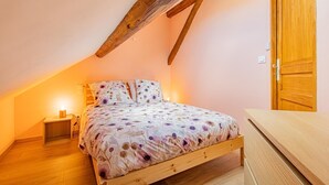 A bedroom with a sloped ceiling, a wooden bed frame, and a nightstand with a lamp. - Le Saint-Loup - DRACY SAINT LOUP (DRACY SAINT LOUP)