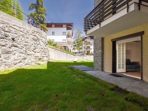 Un appartement moderne doté d’un mur de soutènement en pierre, d’un petit espace verdoyant et offrant une vue sur les bâtiments voisins.