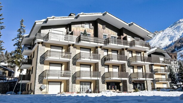 Un hôtel à plusieurs étages doté de balcons, proposant du matériel de ski et offrant une vue sur un paysage montagneux enneigé.