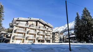 Un hôtel à plusieurs étages, doté de balcons, avec une chaîne de montagnes enneigées en toile de fond.