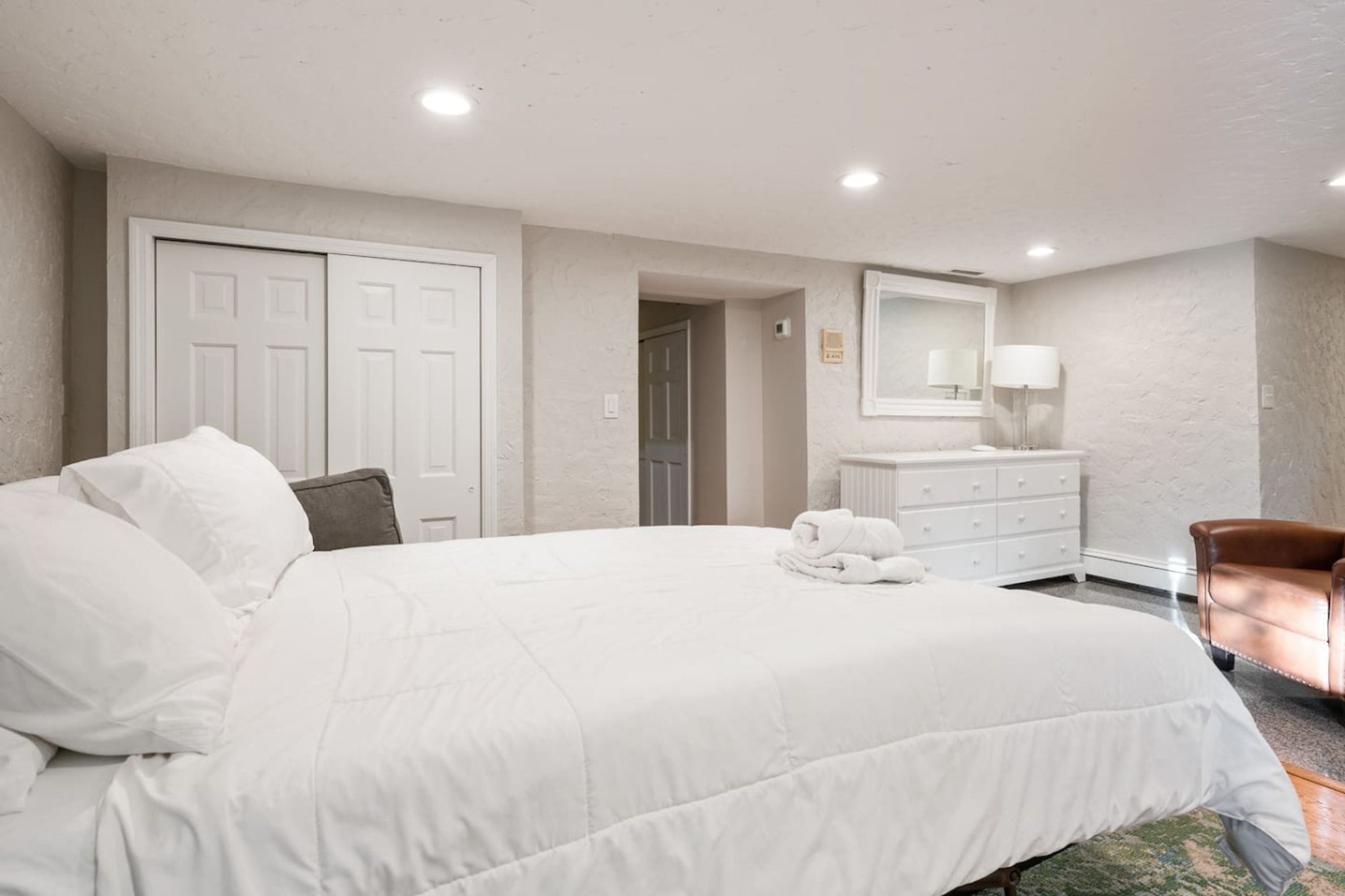 A hotel room with a large bed, a dresser, a chair, and a mirror on the wall.