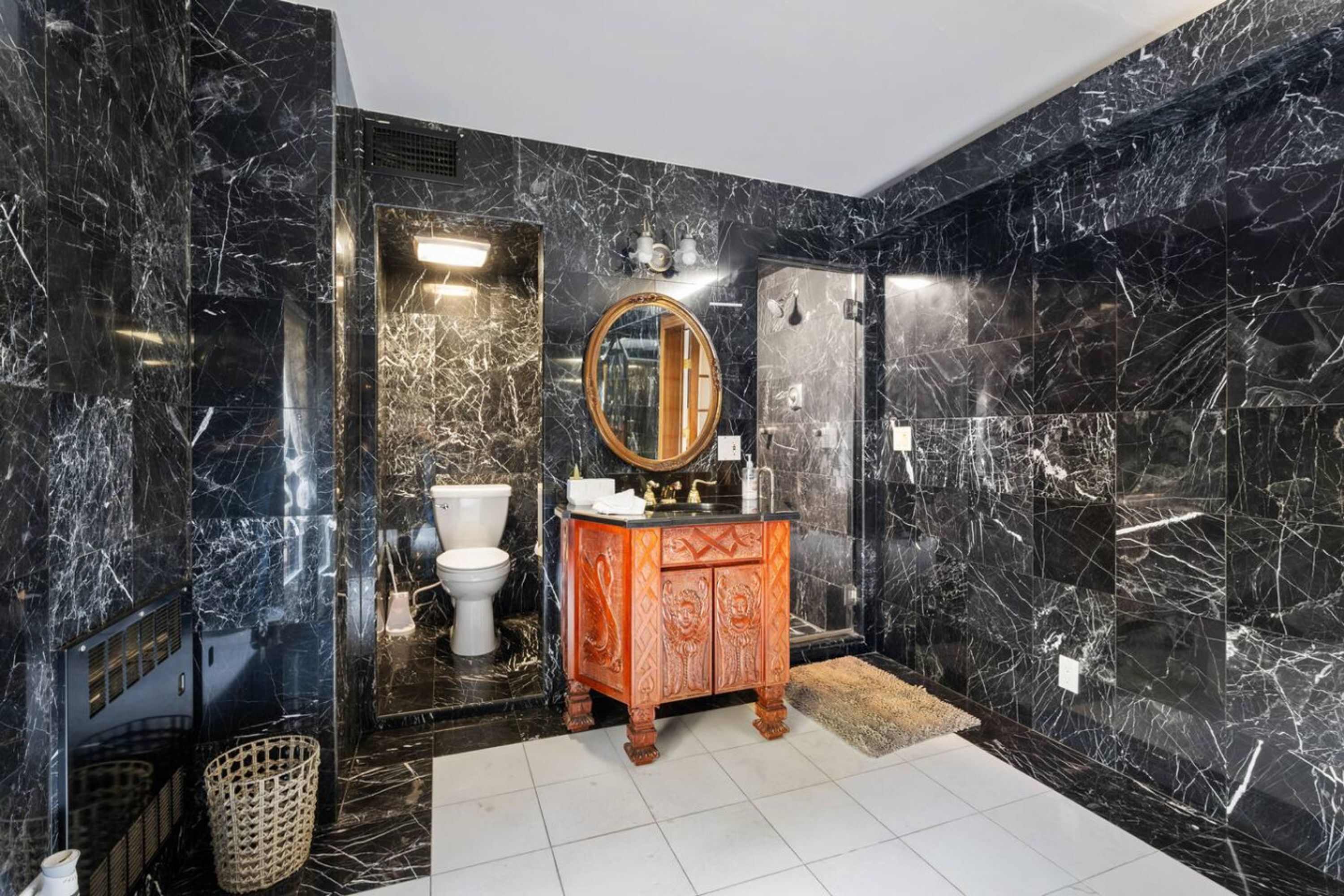 A bathroom with black marble walls, a wooden vanity, a round mirror, and a white toilet.