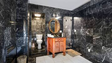 A bathroom with black marble walls, a wooden vanity, a round mirror, and a white toilet.
