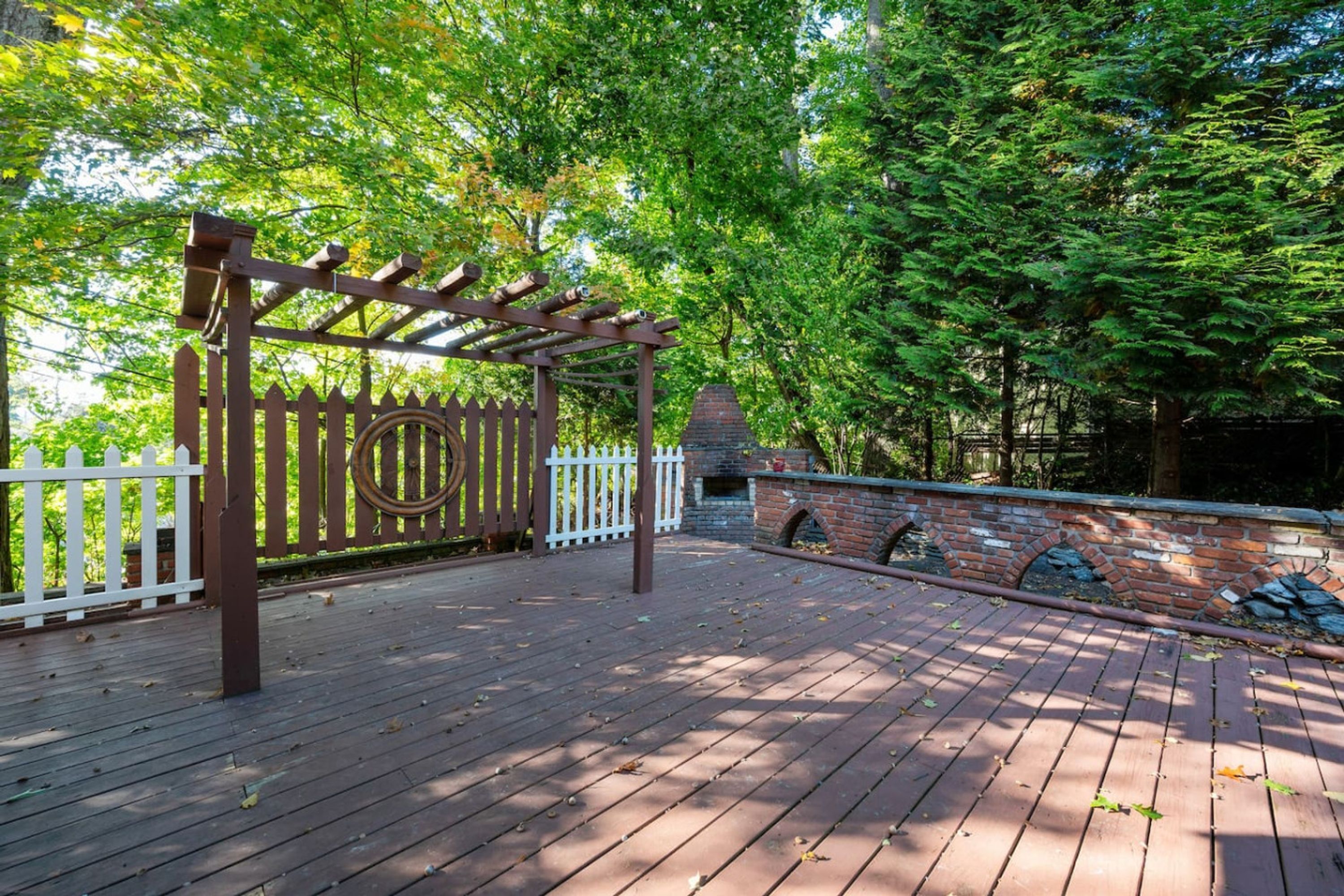 A wooden deck with a pergola and a brick wall.
