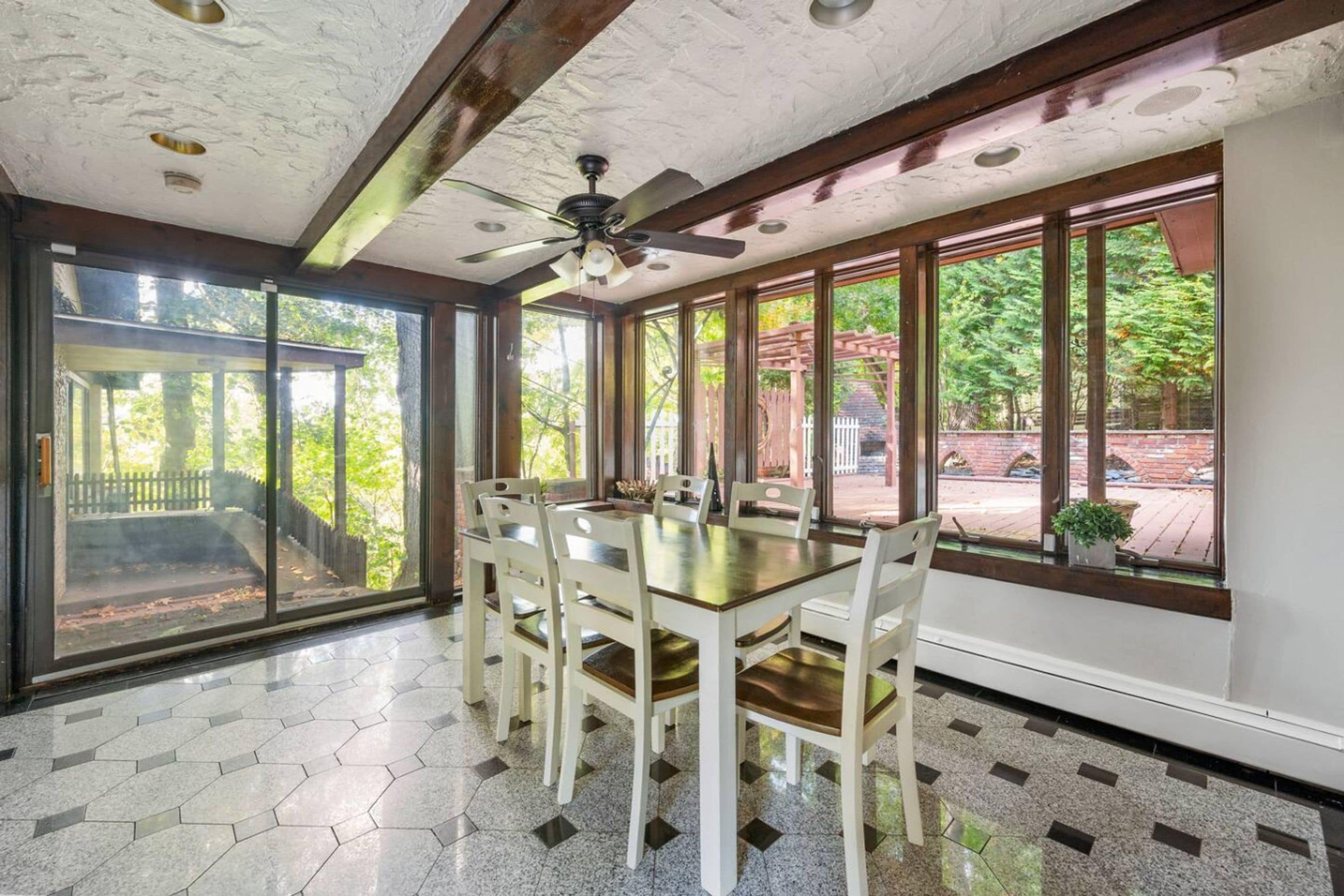 Un comedor con una mesa grande y sillas, ventanas amplias con vistas a zonas verdes y un ventilador de techo.