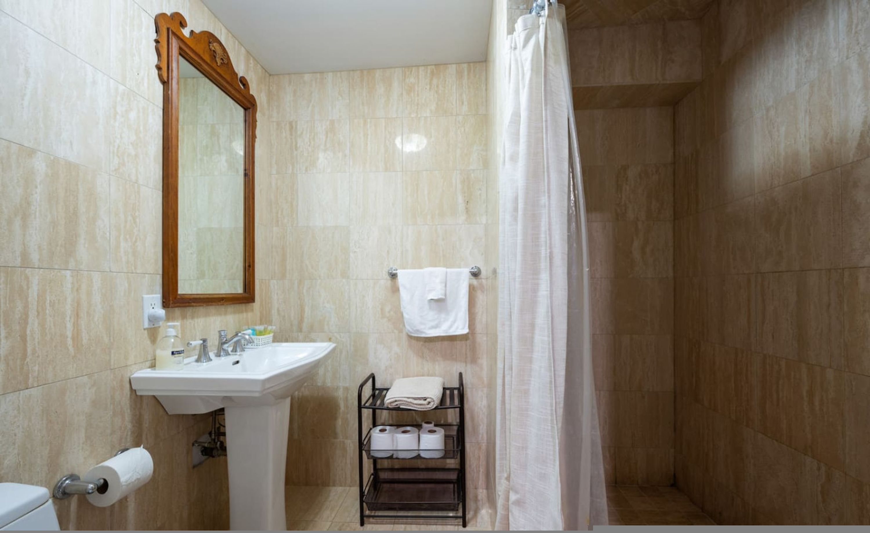 Ein Badezimmer mit Waschbecken, Spiegel, Toilettenpapier, Handtuchhalter und Duschvorhang.