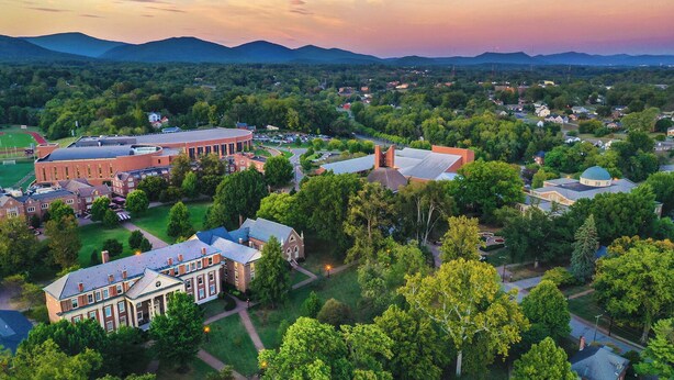 An aerial view of a campus with multiple buildings, including a large brick structure and several smaller houses, surrounded by greenery and a mountainous backdrop. - Free Garage + King Bed - Brick Loft in Downtown Roanoke - Walk to everything (Roanoke)