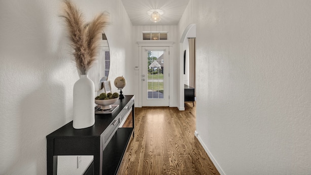 Un couloir doté d’un plancher en bois, de murs blancs et d’une porte donnant sur l’extérieur.