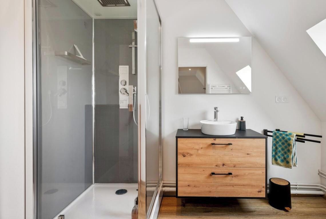 Een moderne badkamer met een glazen douchecabine, een houten wastafelmeubel met een wastafel en een handdoek aan een rek.