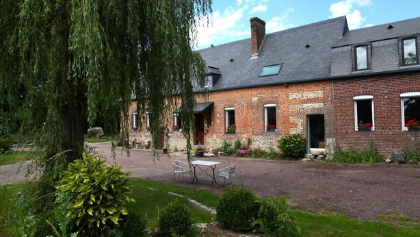 Un bâtiment en briques avec une cour, une table et des chaises, et un grand arbre.