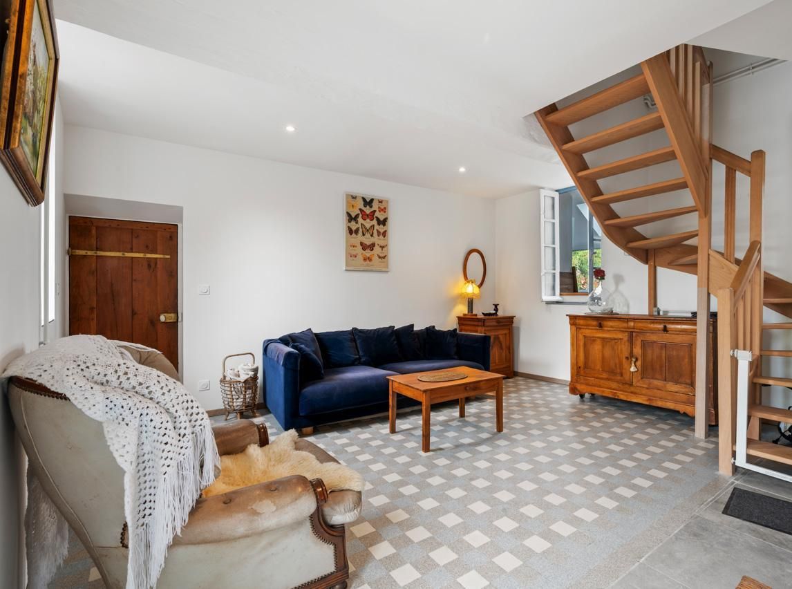 Een woonkamer met een blauwe bank, een houten salontafel en een geruite vloer. Op de achtergrond is een houten trap te zien.