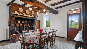 Une salle à manger rustique avec des poutres apparentes, une cheminée en briques et une table dressée pour quatre personnes.