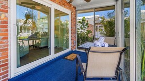 Une terrasse couverte avec une table et des chaises, un ventilateur de plafond et de grandes fenêtres offrant une vue sur les environs.