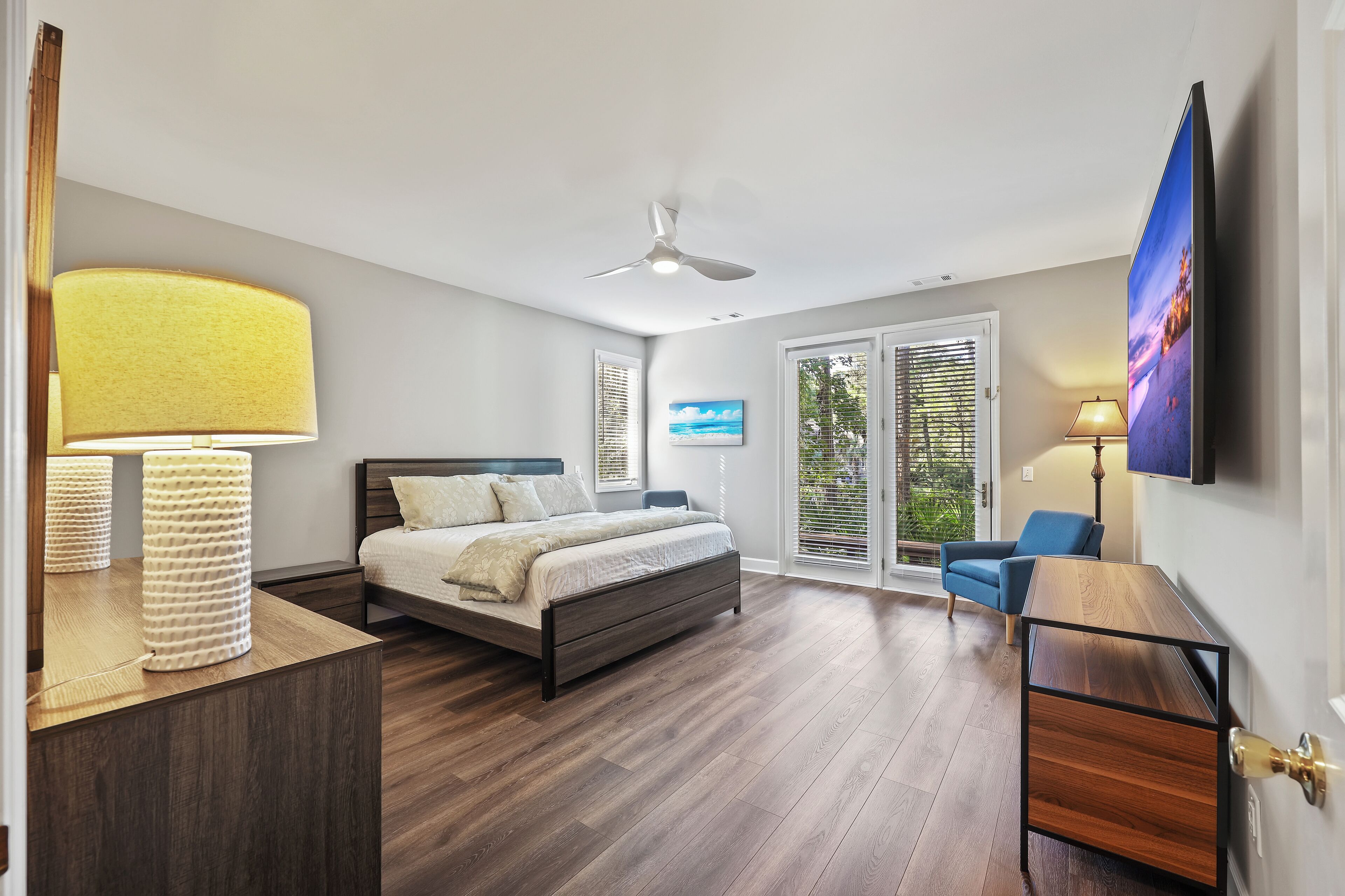 Bedroom 1: Primary suite with 1 King bed, two arm chairs, access to the back pool deck, Smart TV, en-suite bathroom includes walk-in shower, double vanity, and separate soaking tub
