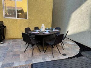 Eine Terrasse im Freien mit einem runden Tisch und Stühlen, einer weißen Karaffe und blauem Glas.
