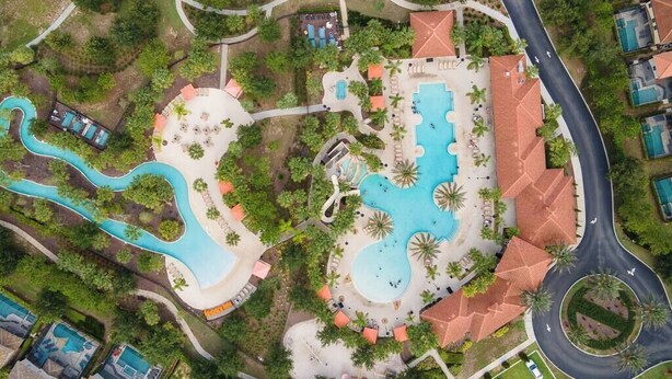 An aerial view of a resort with multiple swimming pools, a winding water feature, and a central building with a red-tiled roof. - Fabulous 5 BR With Pool Solterra Resort (Davenport)