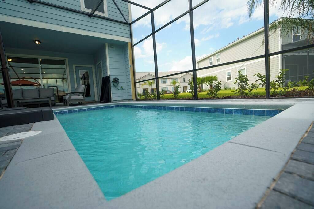 An indoor swimming pool with clear blue water, surrounded by a glass enclosure, and a patio area with outdoor furniture.