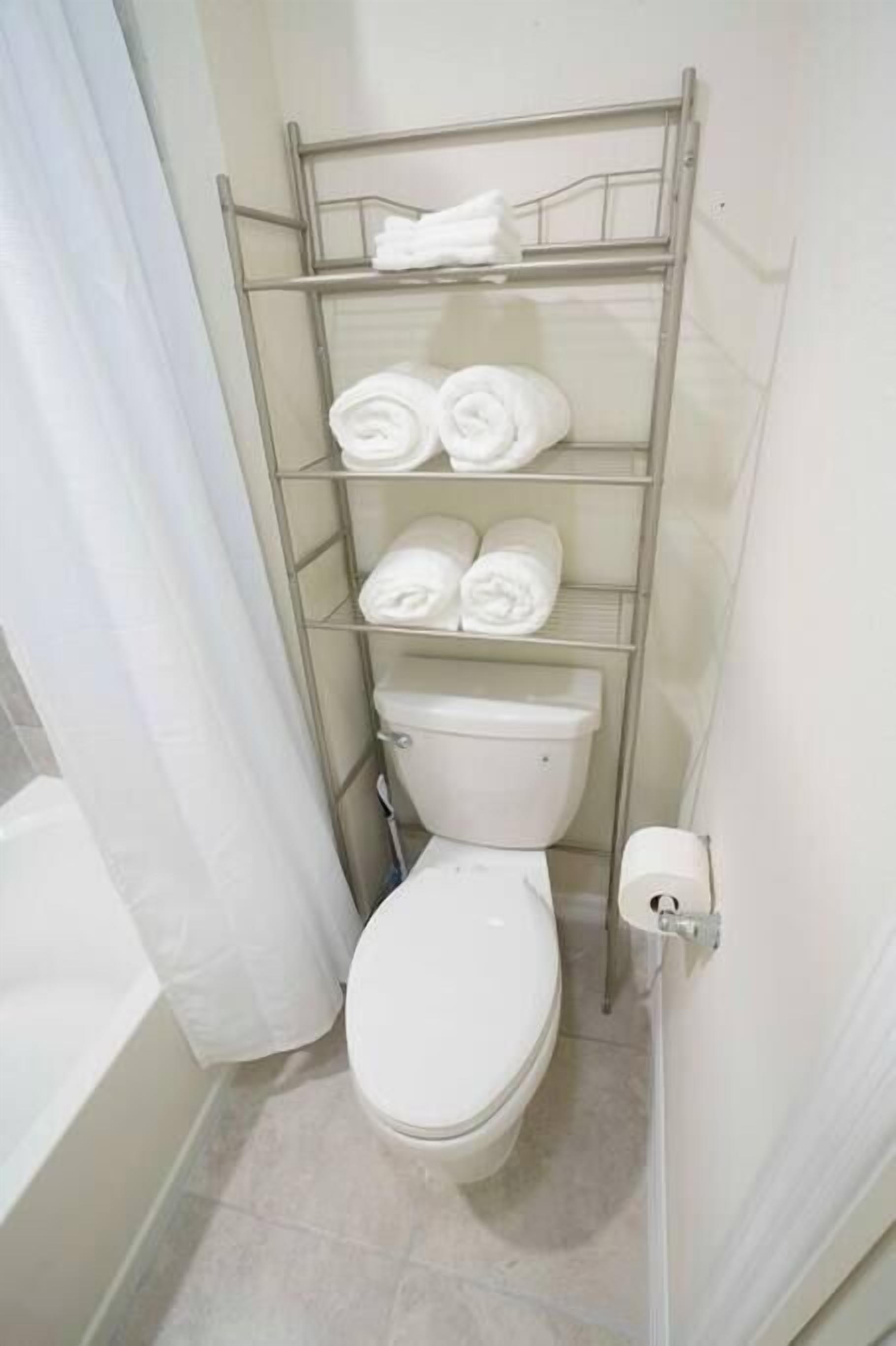 Un baño compacto con inodoro, una estantería metálica con toallas y un dispensador de papel higiénico.