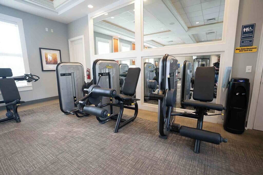 A gym with various exercise machines, a mirror, and a sign indicating restrooms.