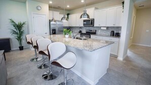 A modern kitchen with white cabinets, granite countertops, stainless steel appliances, and bar stools. - Fabulous 5 BR With Pool Solterra Resort (Davenport)