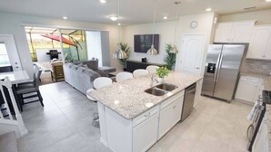 A modern kitchen with a central island, stainless steel appliances, and a dining area with a sofa and chairs. - Fabulous 5 BR With Pool Solterra Resort (Davenport)