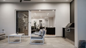 A modern living room with a sofa, a coffee table, and a kitchen area with a stove. - Belle Escapes - Henley Beach House (Henley Beach)