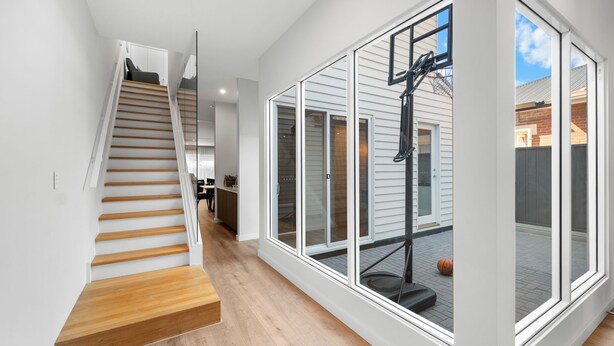 A modern interior with a wooden staircase, a basketball hoop, and large windows. - Belle Escapes - Henley Beach House (Henley Beach)