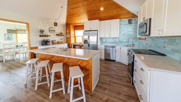 Een moderne keuken met een houten plafond, witte kastjes en een centraal eiland met krukken.