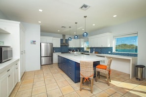 A modern kitchen with a large island, stainless steel appliances, and a view of the sea.